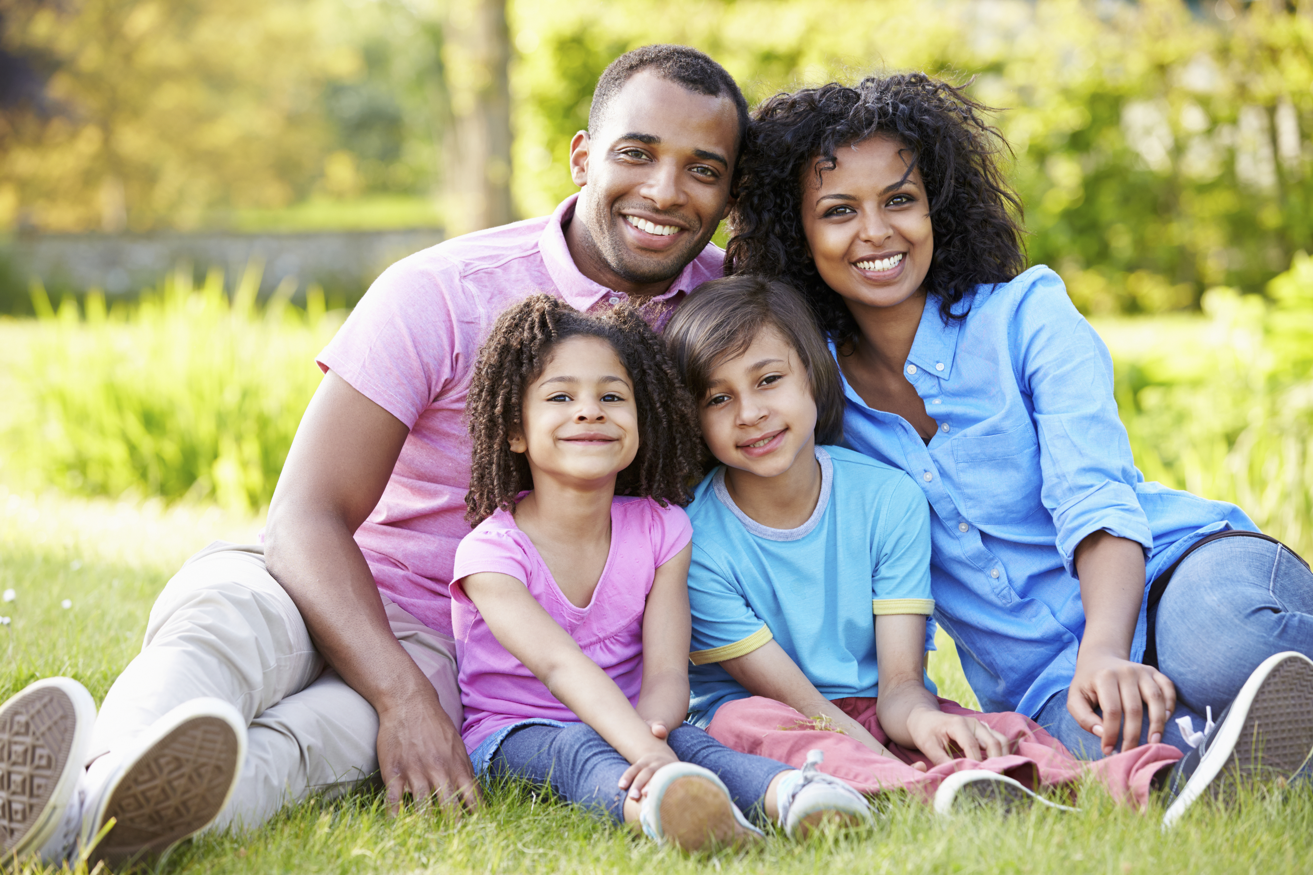 African American Family Sitting In Garden Smiling At Camera